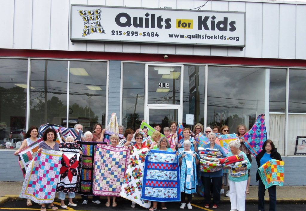 Quilts for Kids staff gathered outside headquarters holding finished quilts.