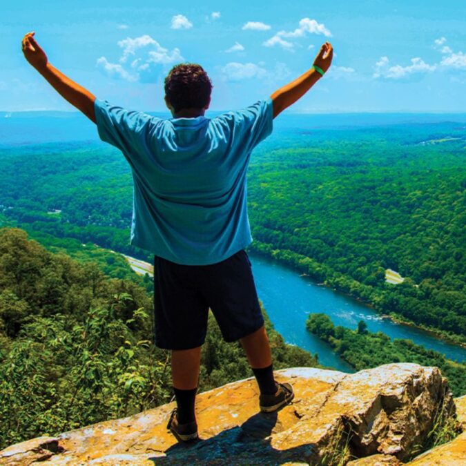 A teenage boy at the top of a cliff he was hiking, raising his arms to the sky