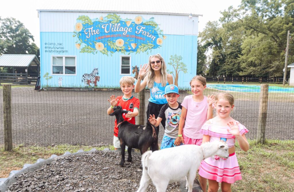 Camp NAC Director, Brianne Feinour waves with four little campers and two goats. 