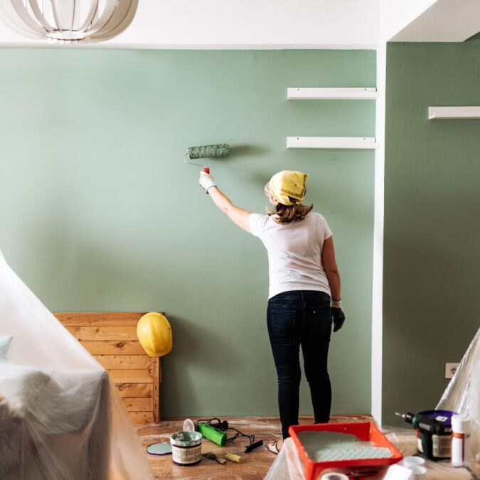 A woman with a head scarf, paints a room green. This is a budget-friendly home upgrade.
