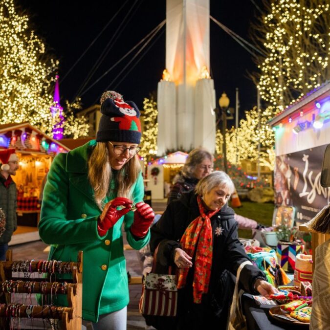 Ladies shop outdoor vendors amid holiday lights at the Easton Winter Village.