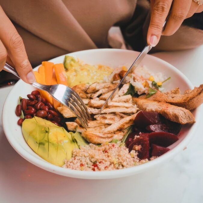 A woman's hands hold utensils over a to go meal.