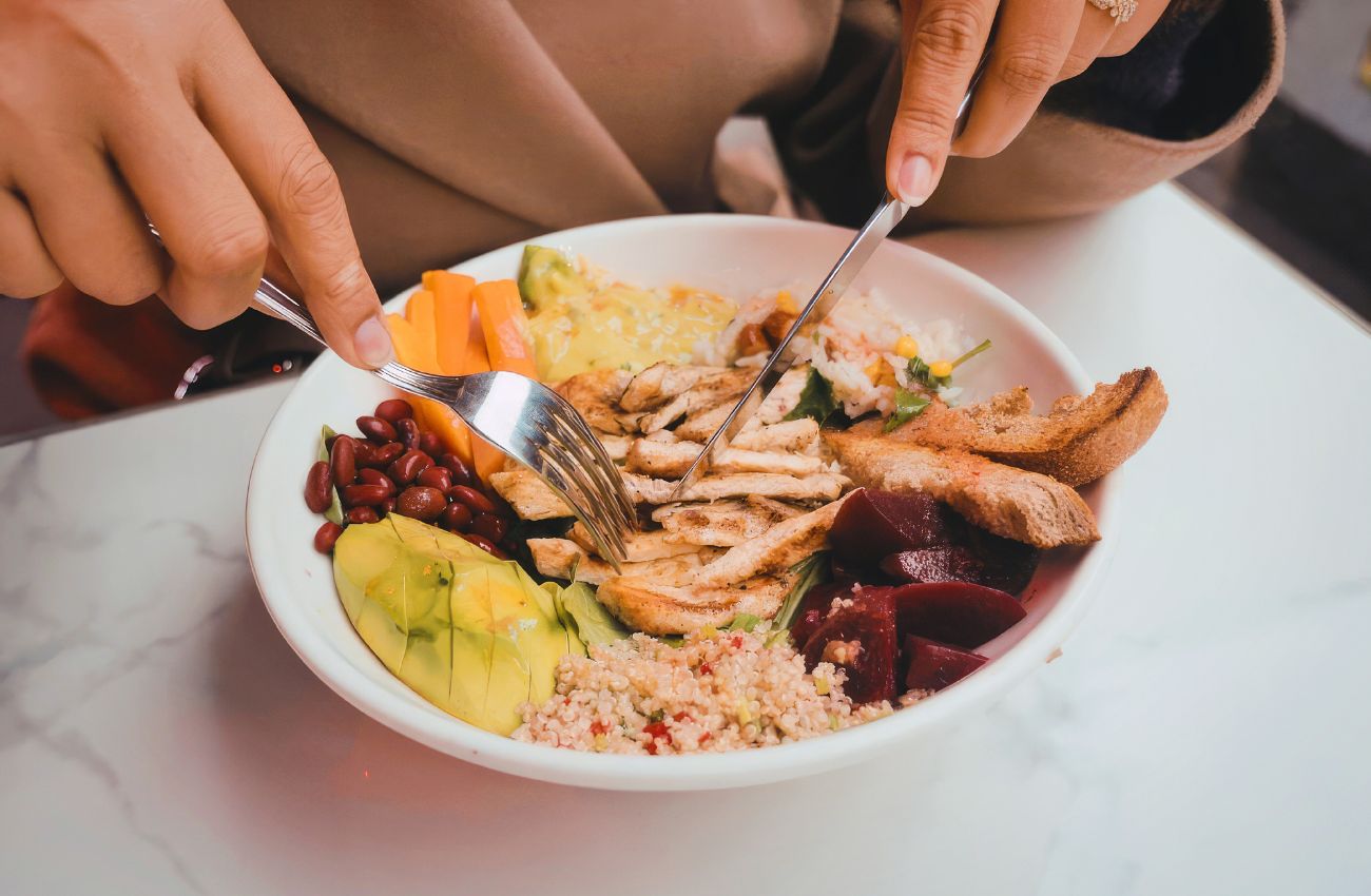 A woman's hands hold utensils over a to go meal.