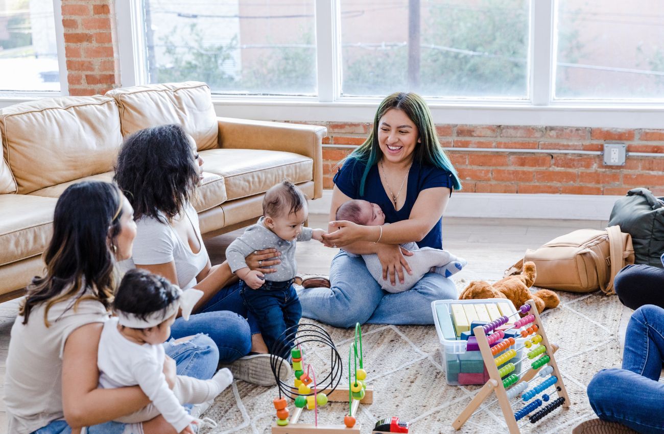 A new parent group of moms sits in a circle on the floor with their babies.