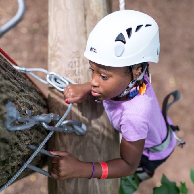 A camper climbs a tree is full gear and helmet at Camp Speers YMCA.