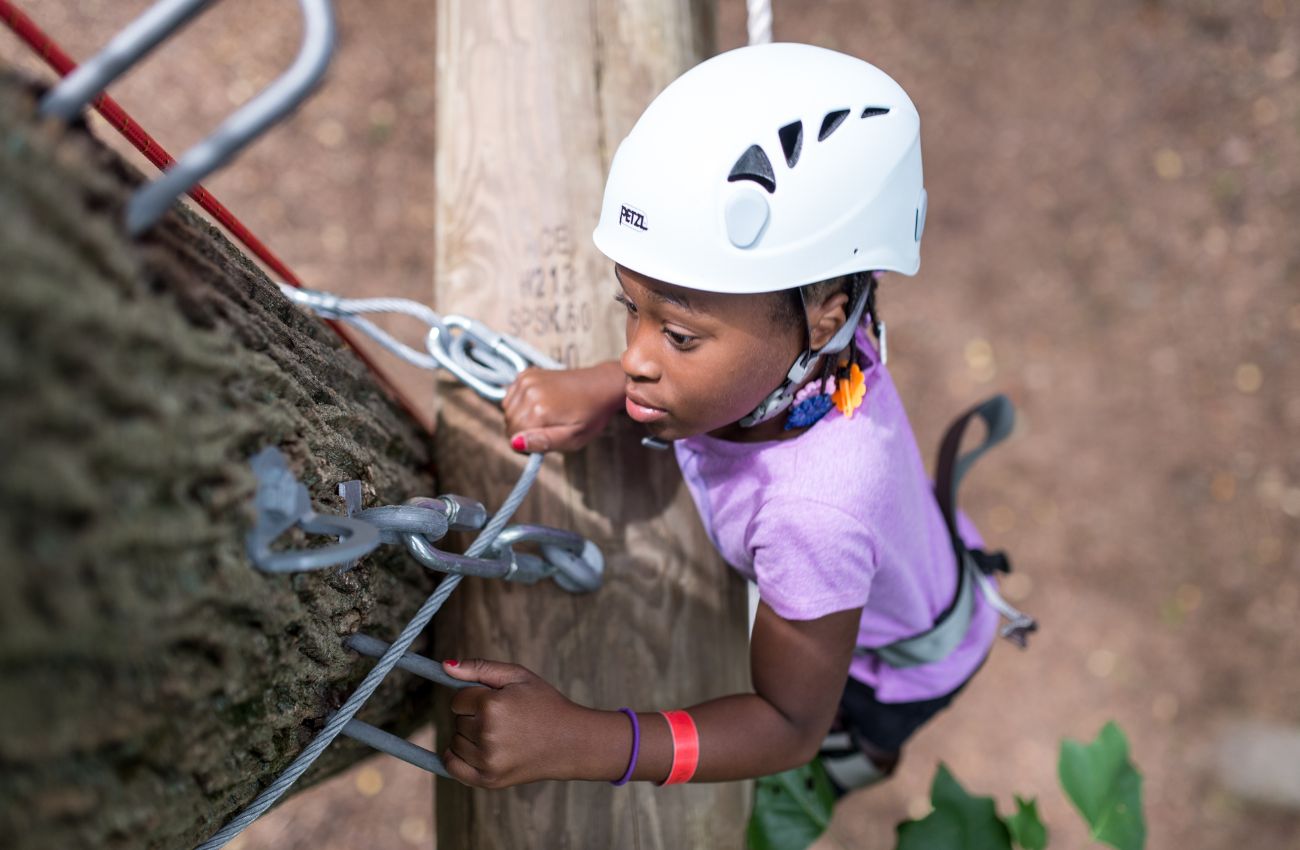 A camper climbs a tree is full gear and helmet at Camp Speers YMCA.