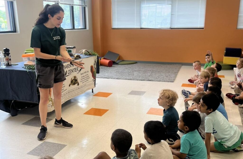 Preschool camp kids gather on the floor to look at a wildlife presenter holding a snake at Celebree School of Warrington.