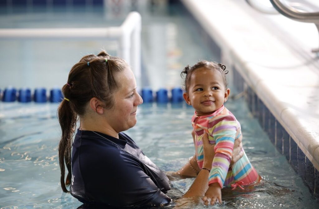A swim instructor holds a happy toddler girl in the water at Big Blue Swim School.