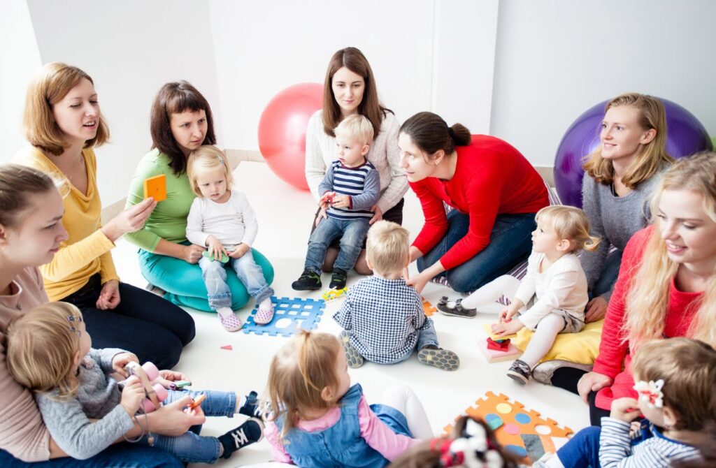 A group of women sit in a cirlcle with their toddler children in a mommy and me class. 