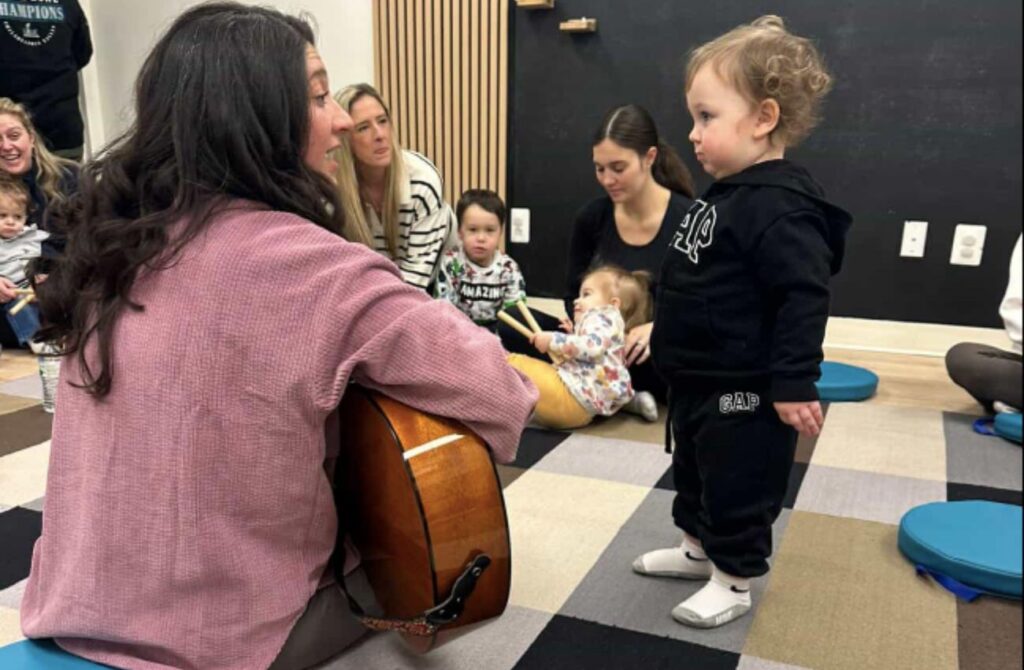 A toddler looks at a music class instructor holding a guitar at New Groove Music Studio in Holland, PA.