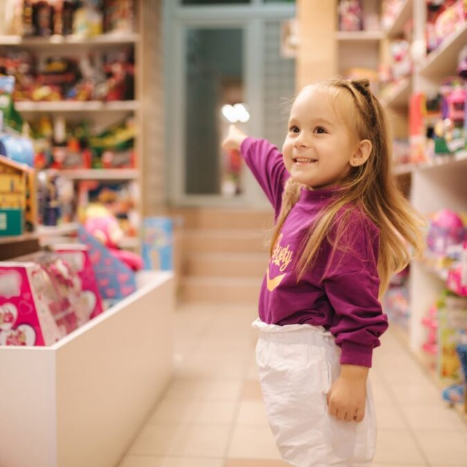 A little girl points at all the toys in a local toy store.